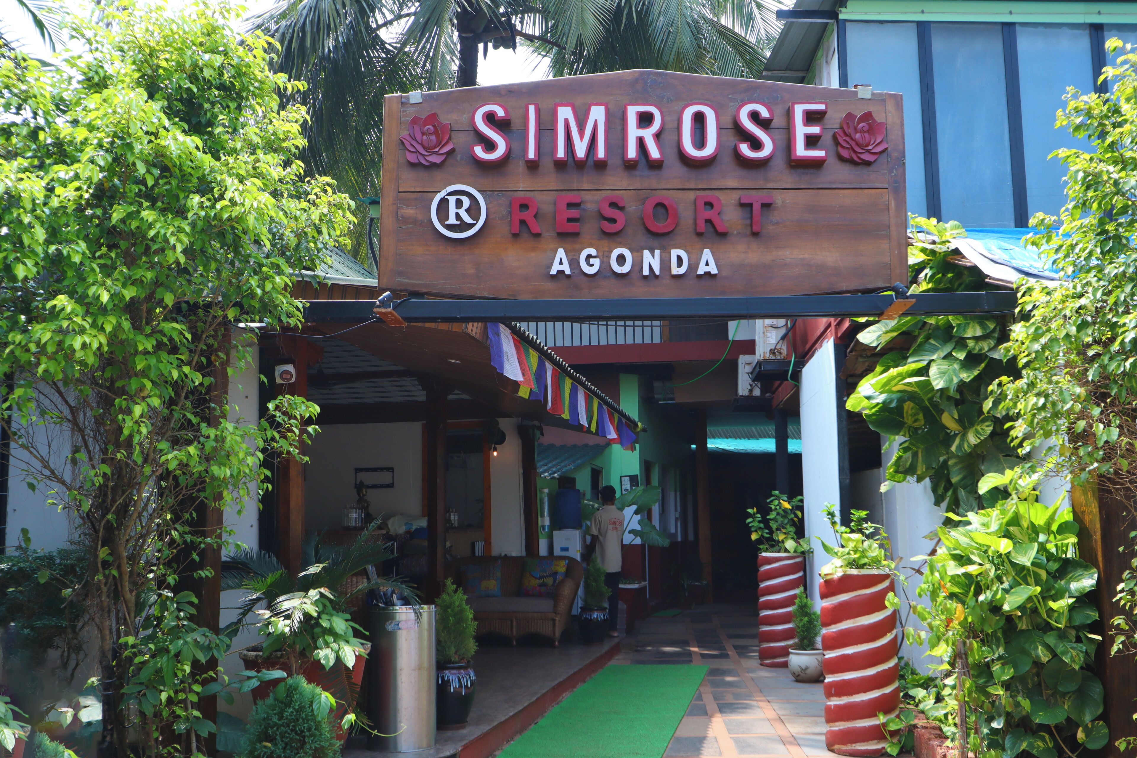 Un letrero de madera para el Simrose Resort en Agonda, con un logotipo y el nombre del resort.