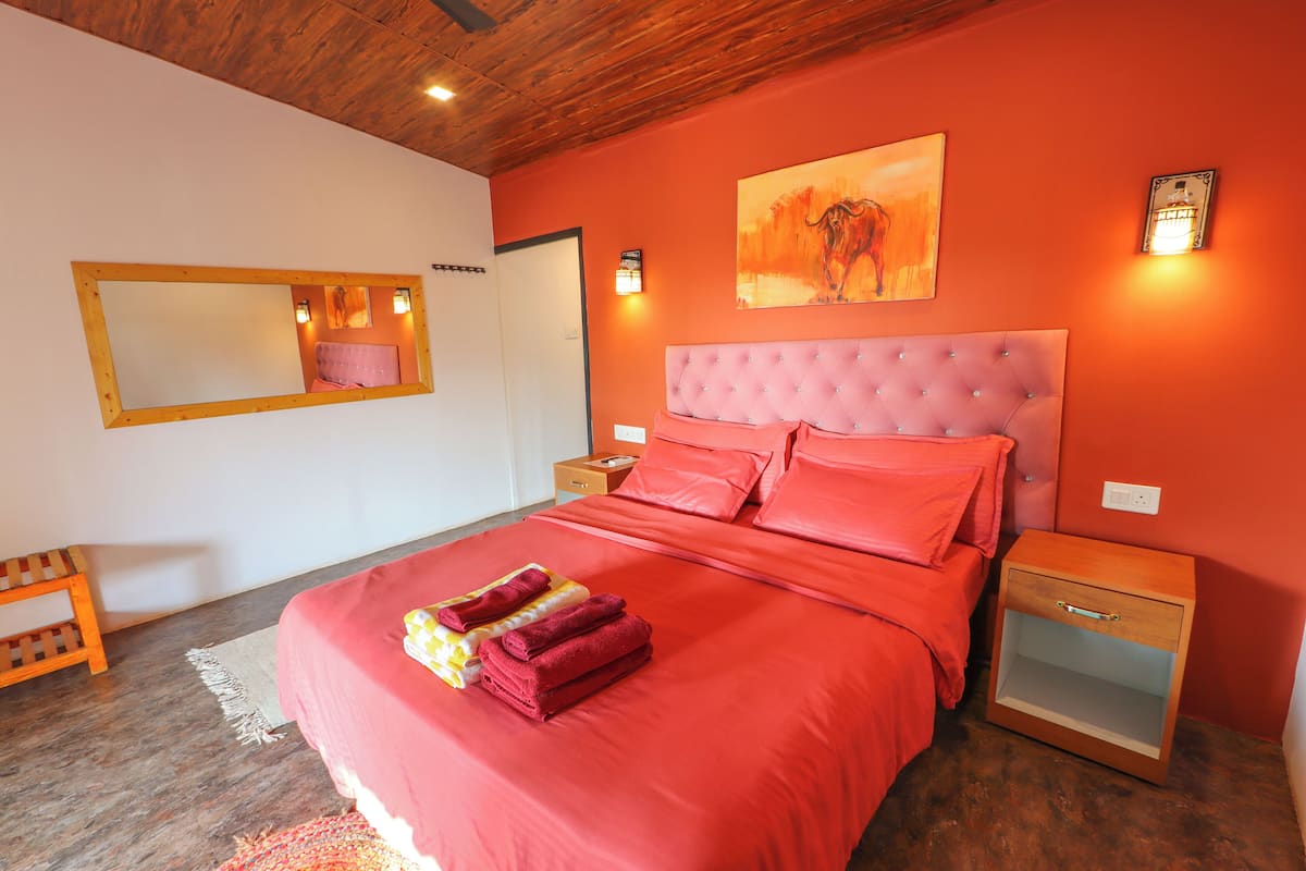 Quarto com cama grande, mesa de cabeceira de madeira, espelho e luminária na parede.