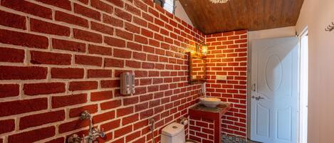 A bathroom with a red brick wall, a white toilet, a sink, and a wooden ceiling.