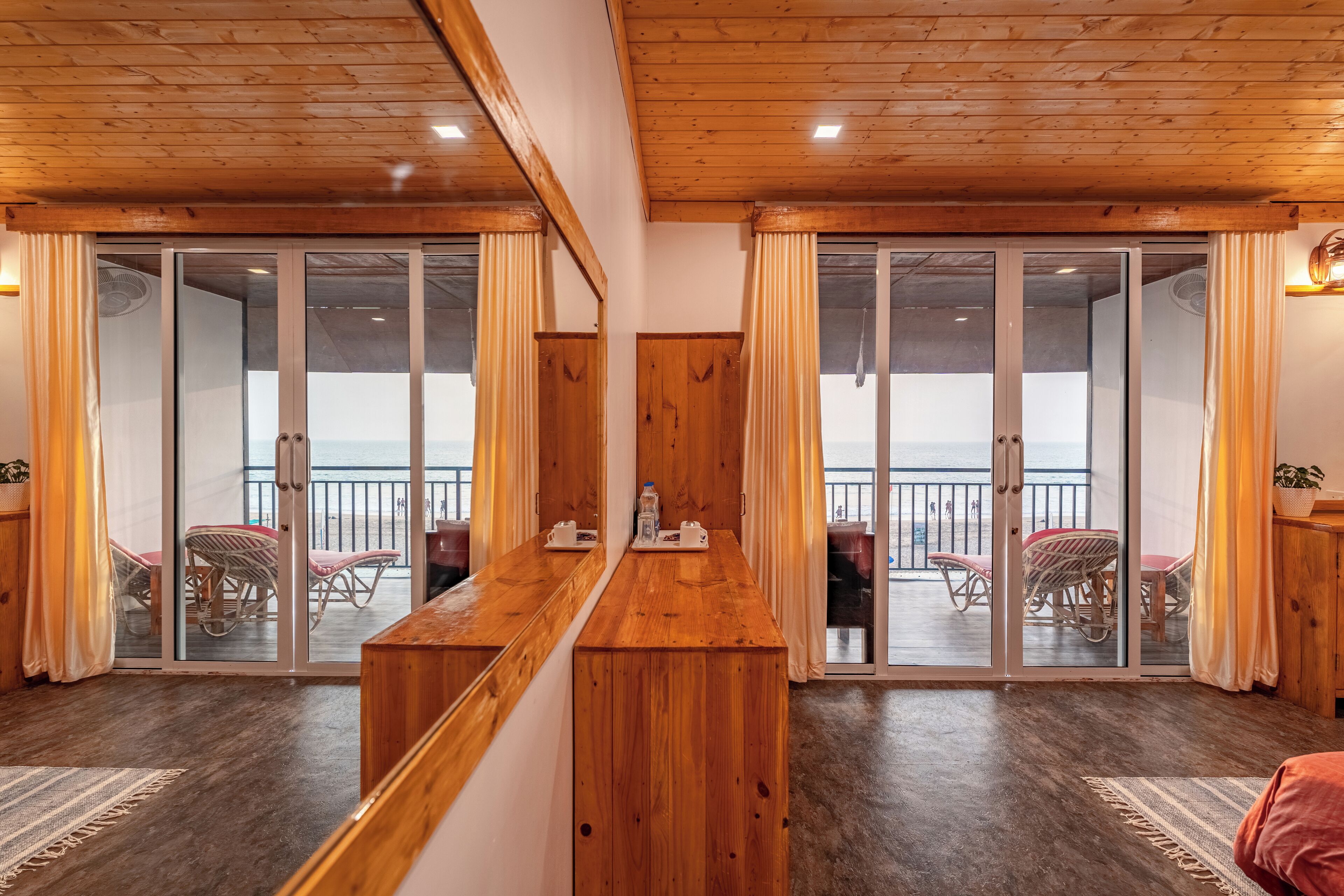 A wooden interior with a long table, sliding glass doors leading to an outdoor seating area with chairs and a table.