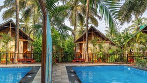 A pool area with two wooden cabins, surrounded by palm trees. - Simrose Resort South End of Agonda Beach (Canacona)