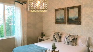 Ein Schlafzimmer mit einem Bett, zwei Bildern, einer Wand mit Muster, einem Fenster mit Vorhängen und einer Hängelampe.