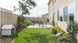Ein Garten mit einem kleinen Gerätehaus, einem Patio-Tisch und Stühlen.