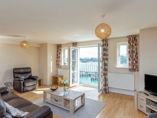 A living room with a sofa, coffee table, TV stand, and a balcony with a view of the sea.