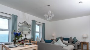 Un salon moderne comprenant un coin repas, un canapé gris, une table à manger en bois et un lustre.