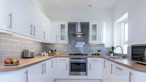 Une cuisine moderne avec des armoires blanches, un plan de travail en bois, un four encastré et une hotte en acier inoxydable.