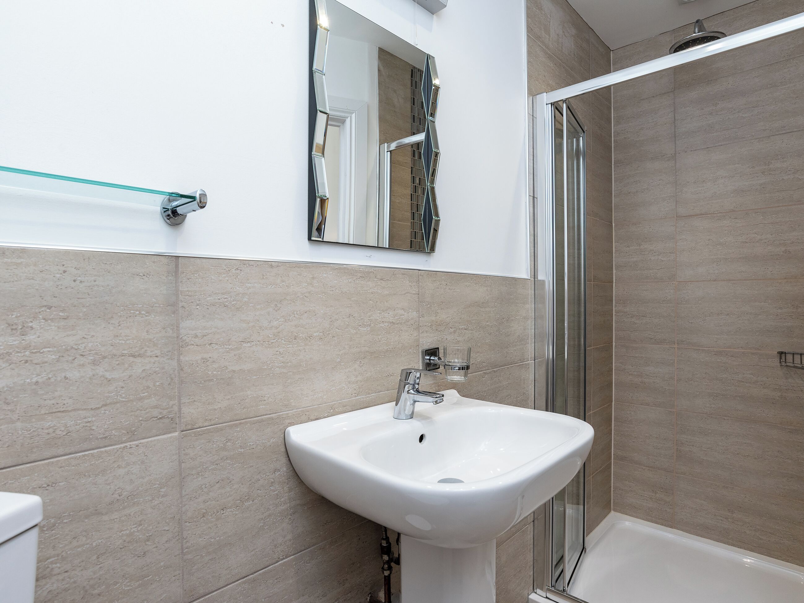 A bathroom with a white sink, a glass shower enclosure, and a mirror above the sink.