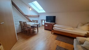 A loft-style room with a dining table, chairs, a sofa, a TV, and a skylight. - Apartment room no. 10 for 1 person (Neuötting)