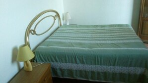 Een enkel bed met een groene gestreepte spreide en een houten hoofdbord. Een klein houten nachtkastje met een lamp staat links van het bed.