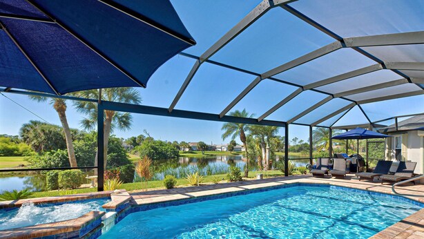 A swimming pool with a view of a lake, surrounded by palm trees and a covered area with lounge chairs. - Bella Vista | Pool | Spa | Lake front | Lounge (Rotonda West)