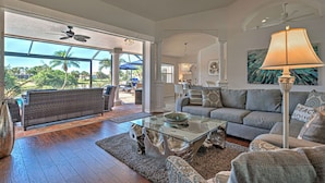 A spacious living room with a glass coffee table, grey sofas, and a view of a pool and palm trees. - Bella Vista | Pool | Spa | Lake front | Lounge (Rotonda West)
