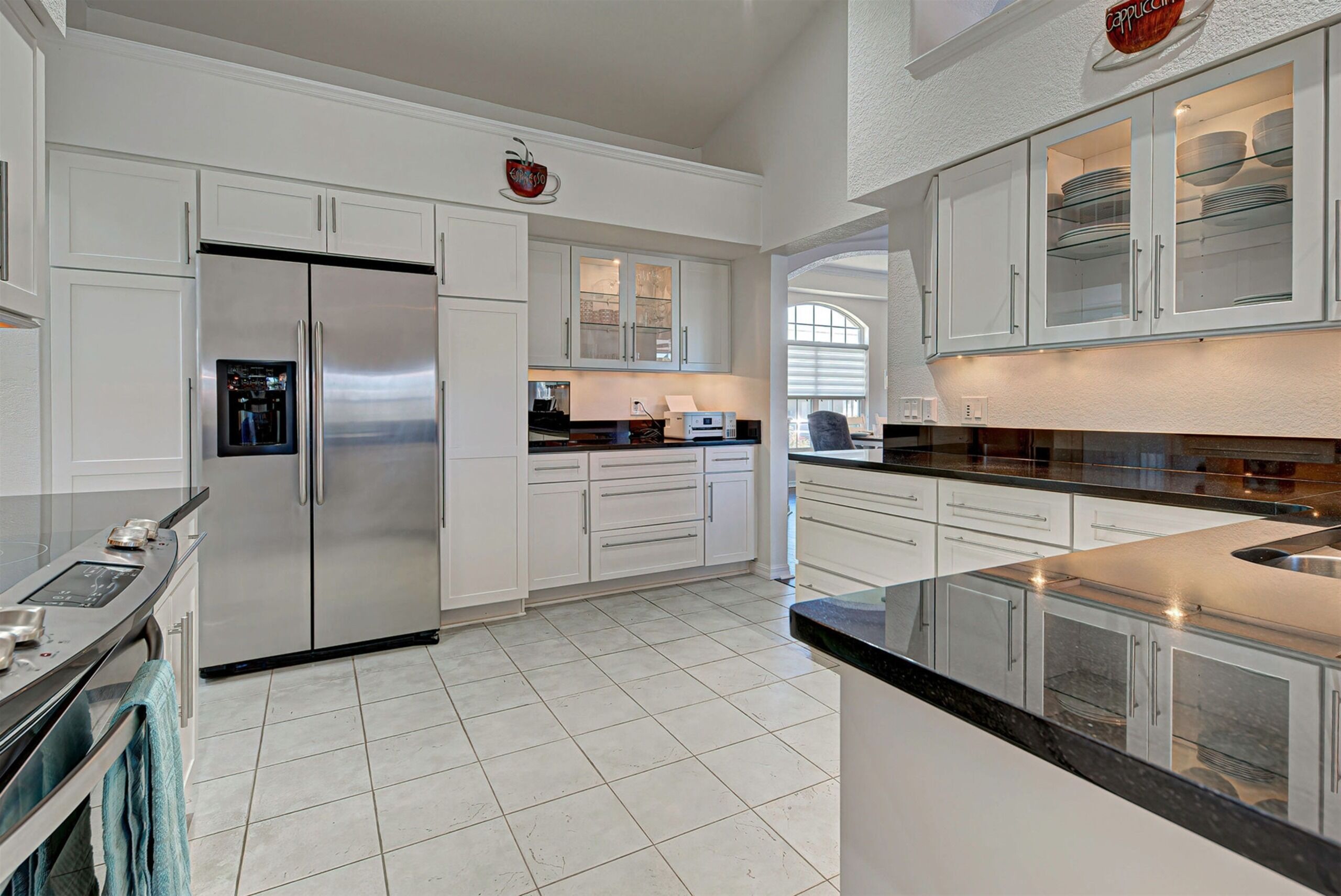 A modern kitchen with stainless steel appliances, white cabinetry, and a large island with a black countertop.
