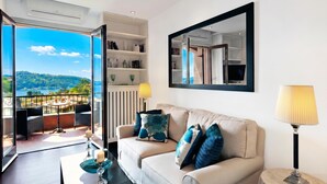 Een woonkamer met een bank, een salontafel, een lamp, een boekenkast en een groot raam met uitzicht op een balkon en het landschap.