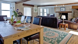 Een eetgedeelte met een houten tafel, stoelen en een vaas met bloemen. Achtergrond is een open haard en een televisie.