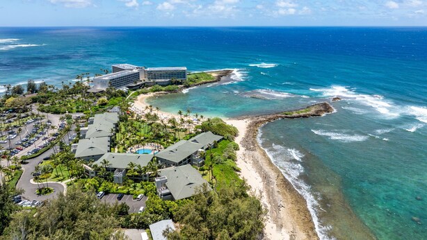 Eine Luftaufnahme eines Küstenresorts mit mehreren Gebäuden, einem Strand und klarem, blauem Wasser.