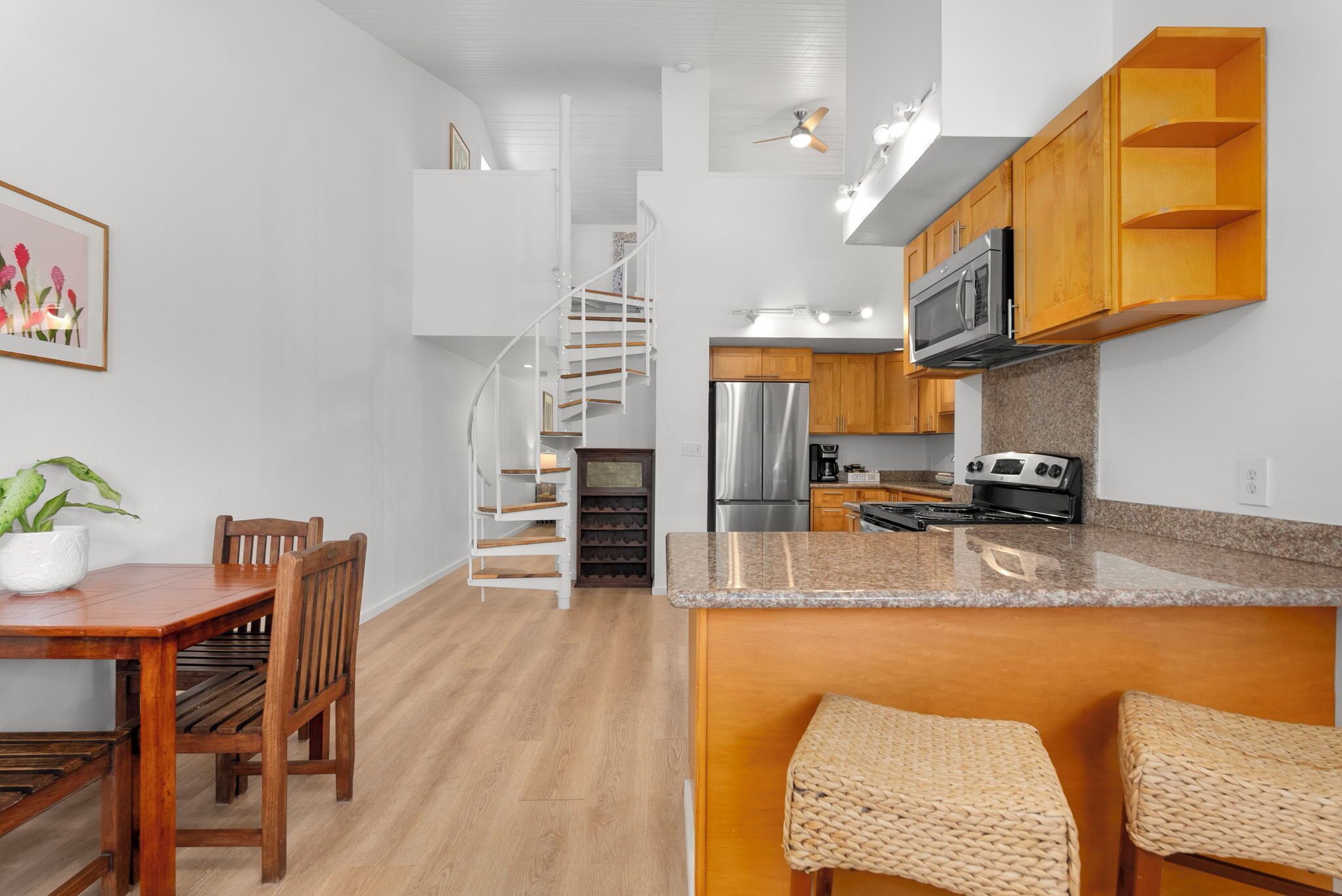 A modern kitchen with a spiral staircase, wooden cabinets, and a granite countertop.
