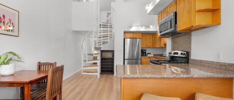 A modern kitchen with a spiral staircase, wooden cabinets, and a granite countertop.