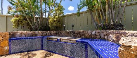 Una piscina con mosaicos azules, rodeada de palmeras y un muro de piedra.