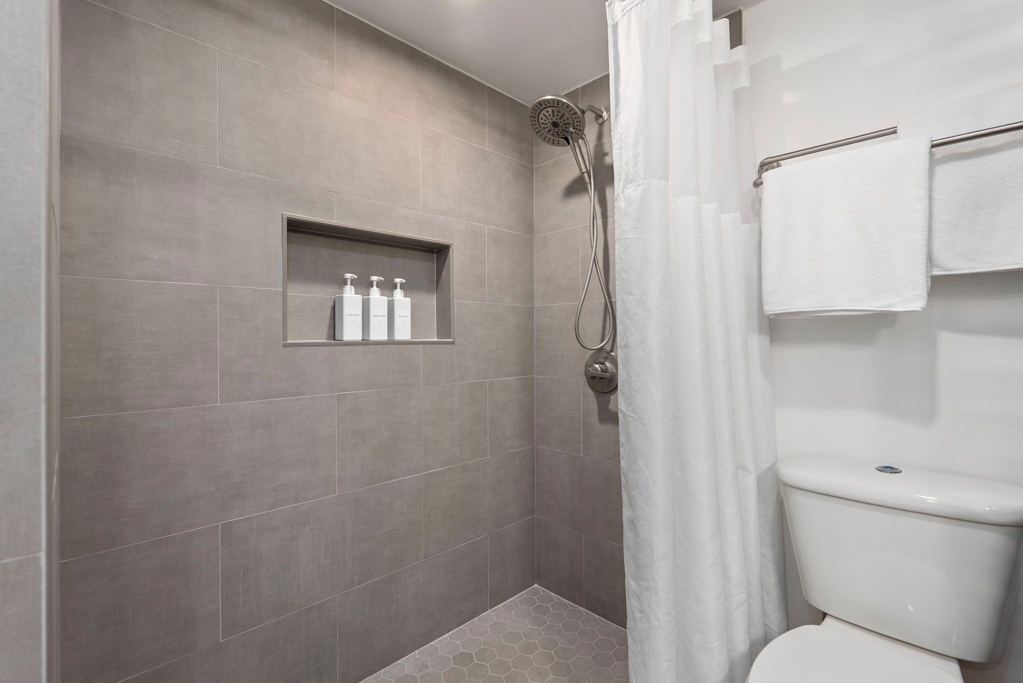 Eine Dusche mit Duschbrause, eine Toilette und ein Ablagefach für Toilettenartikel.