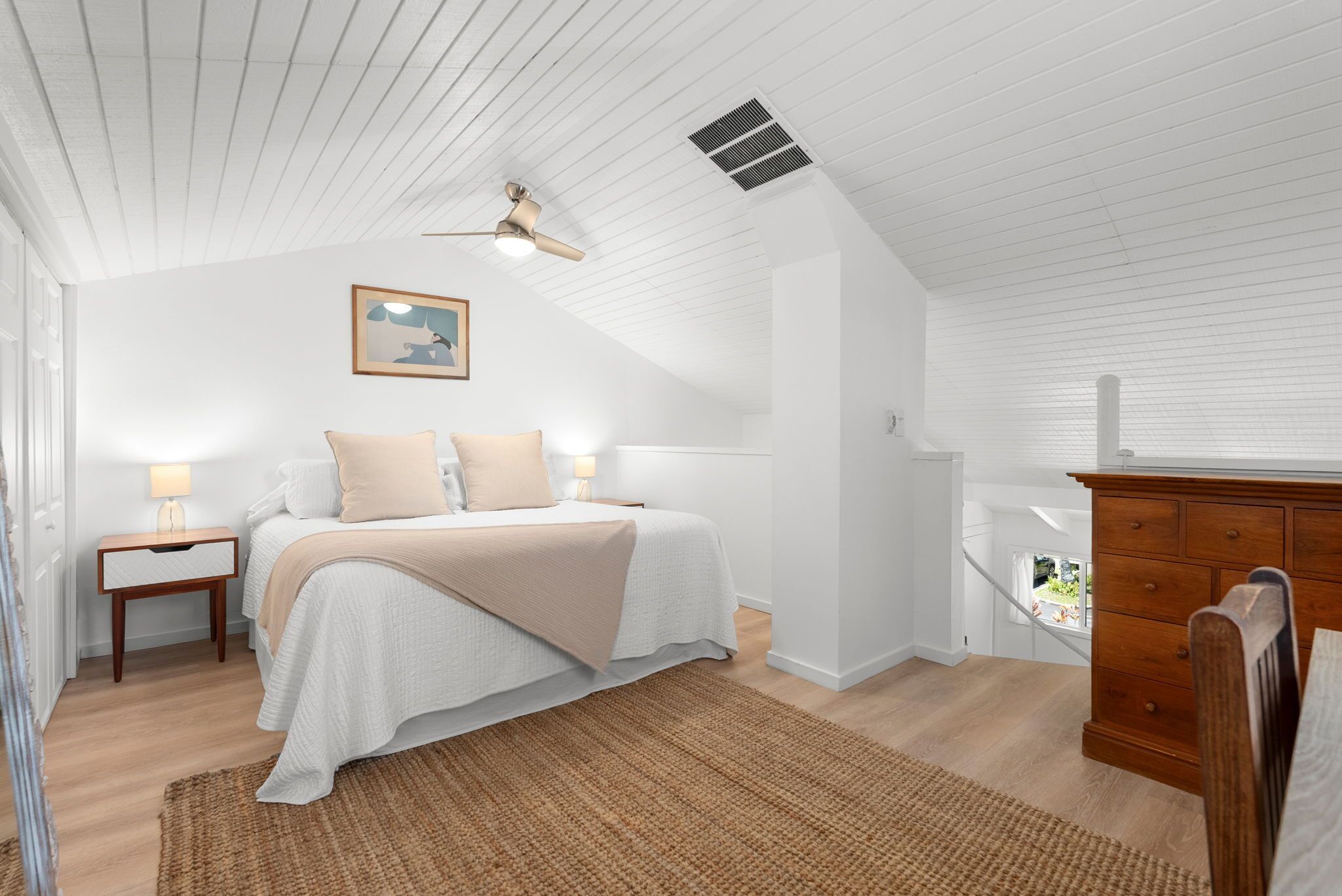 A bedroom with a bed, bedside tables, a dresser, a ceiling fan, and a window.