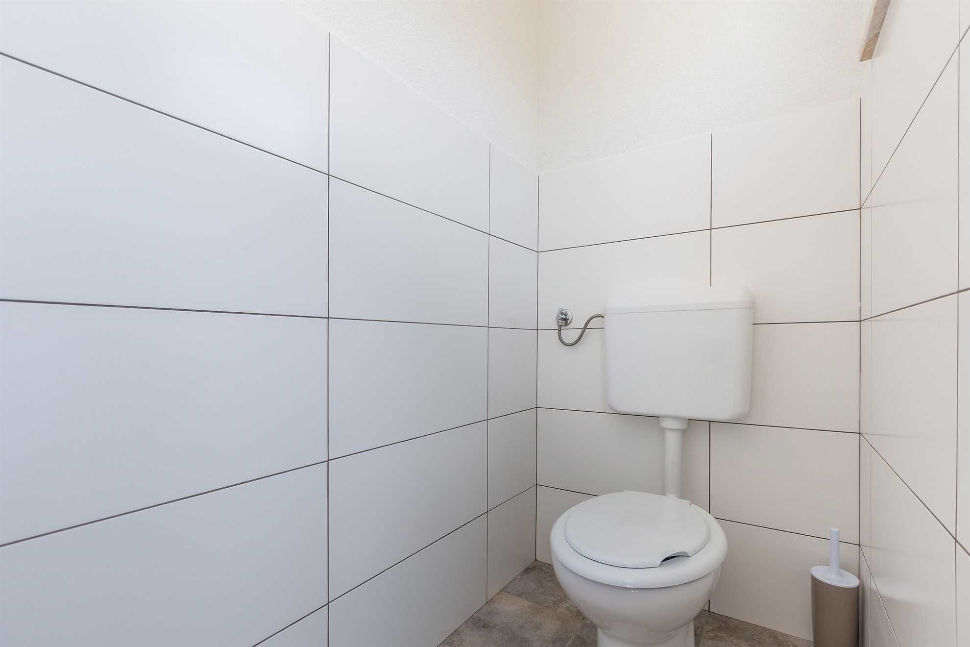 A small, clean bathroom with white tiles, a toilet, and a toilet paper holder.