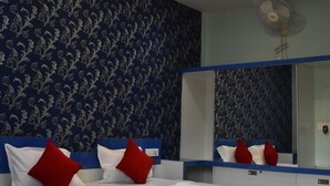 Quarto de hotel com uma cama, almofadas vermelhas e brancas, um espelho e um ventilador de teto.