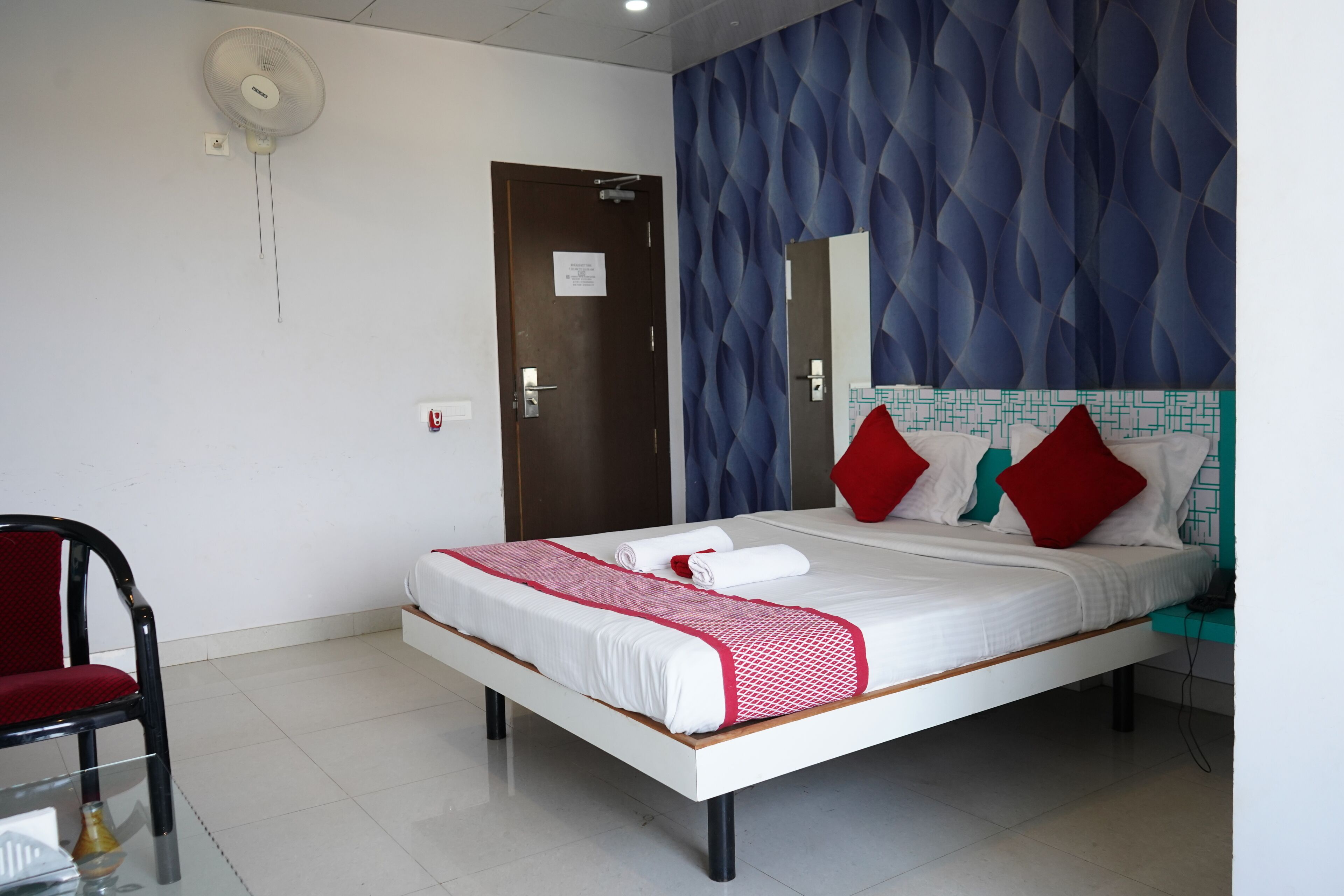 Une chambre d’hôtel équipée d’un lit, d’une chaise, d’un bureau et d’un ventilateur fixé au mur.
