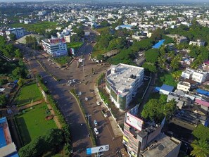 Une vue aérienne d’une ville, avec un bâtiment imposant à toit plat, entouré de verdure et d’autres immeubles.