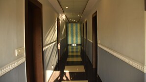 Corredor de hotel com piso xadrez, portas em ambos os lados e parede listrada em azul no final.