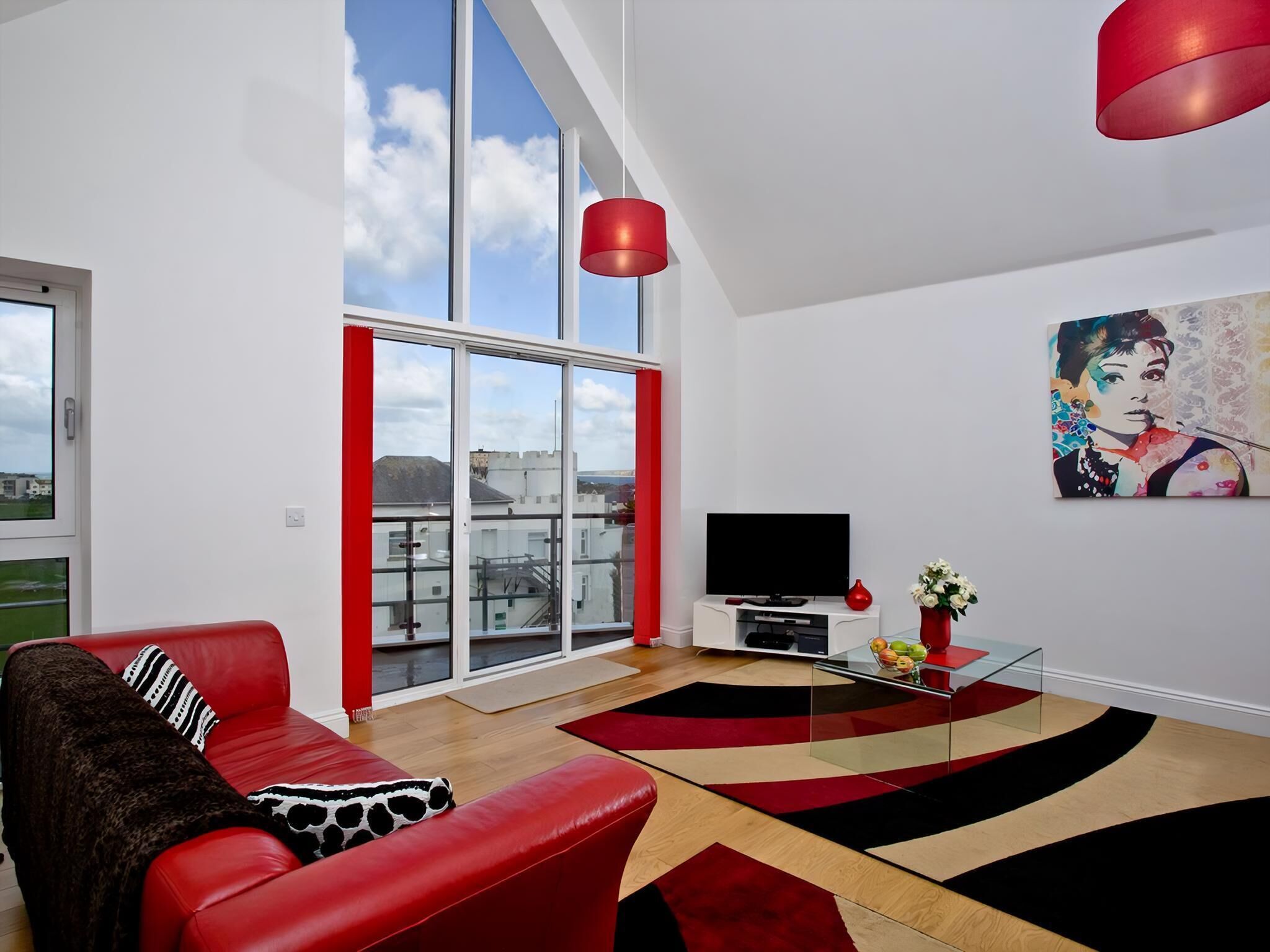 A modern living room with a red sofa, a glass coffee table, and a large window with a view of buildings.