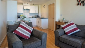 A modern apartment with two grey sofas, a kitchen with white cabinets, a dining table, and a wooden door. - Comfort and luxury in a sea front location with panoramic sea views. (Paignton)