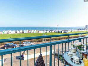 A balcony with a view of the sea, a row of colorful beach huts, and a table with breakfast items.