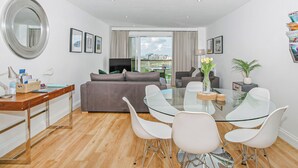 A modern living room with a sofa, a glass dining table with chairs, a TV, and a large mirror.