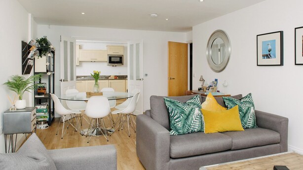 A modern living room with a grey sofa, a coffee table, and a dining area with a glass table and white chairs.