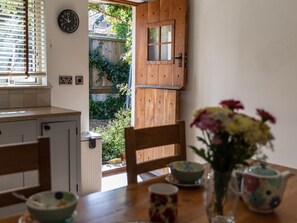 A kitchen with a wooden door leading to a garden, a clock on the wall, and a table with chairs and a vase of flowers. - 2 bedroom accommodation in Totland Bay (Totland Bay)