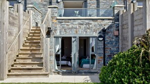 Un bâtiment en pierre de deux étages, doté d’un escalier menant à un balcon, d’une entrée avec une porte vitrée et d’un petit jardin.