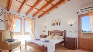 A bedroom with a wooden bed, a chair, a nightstand, and a window with curtains. - Finca with sea views and pool special offer last week of August (Calonge)