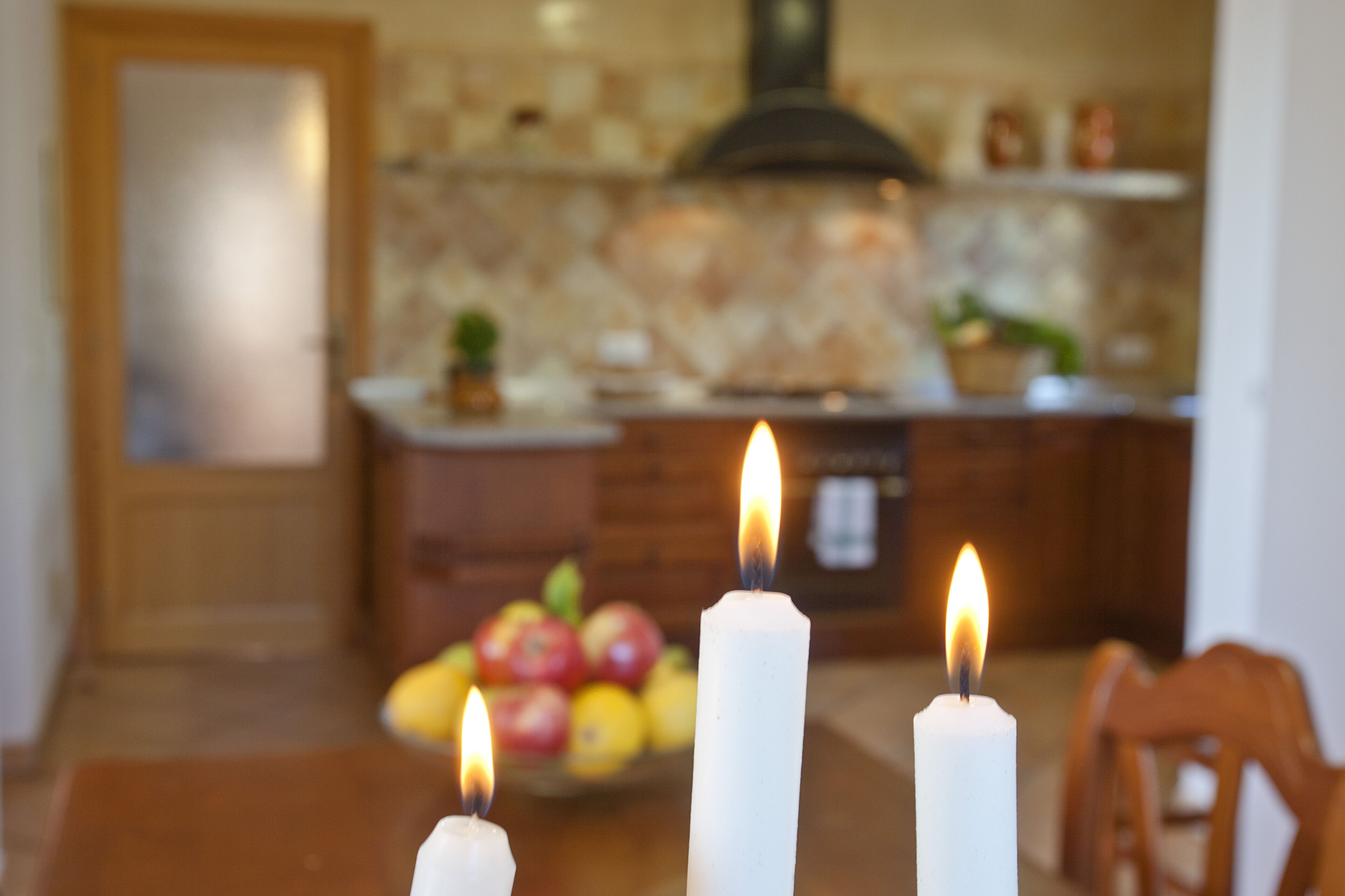 A dining table with three lit candles and a fruit bowl in the background.