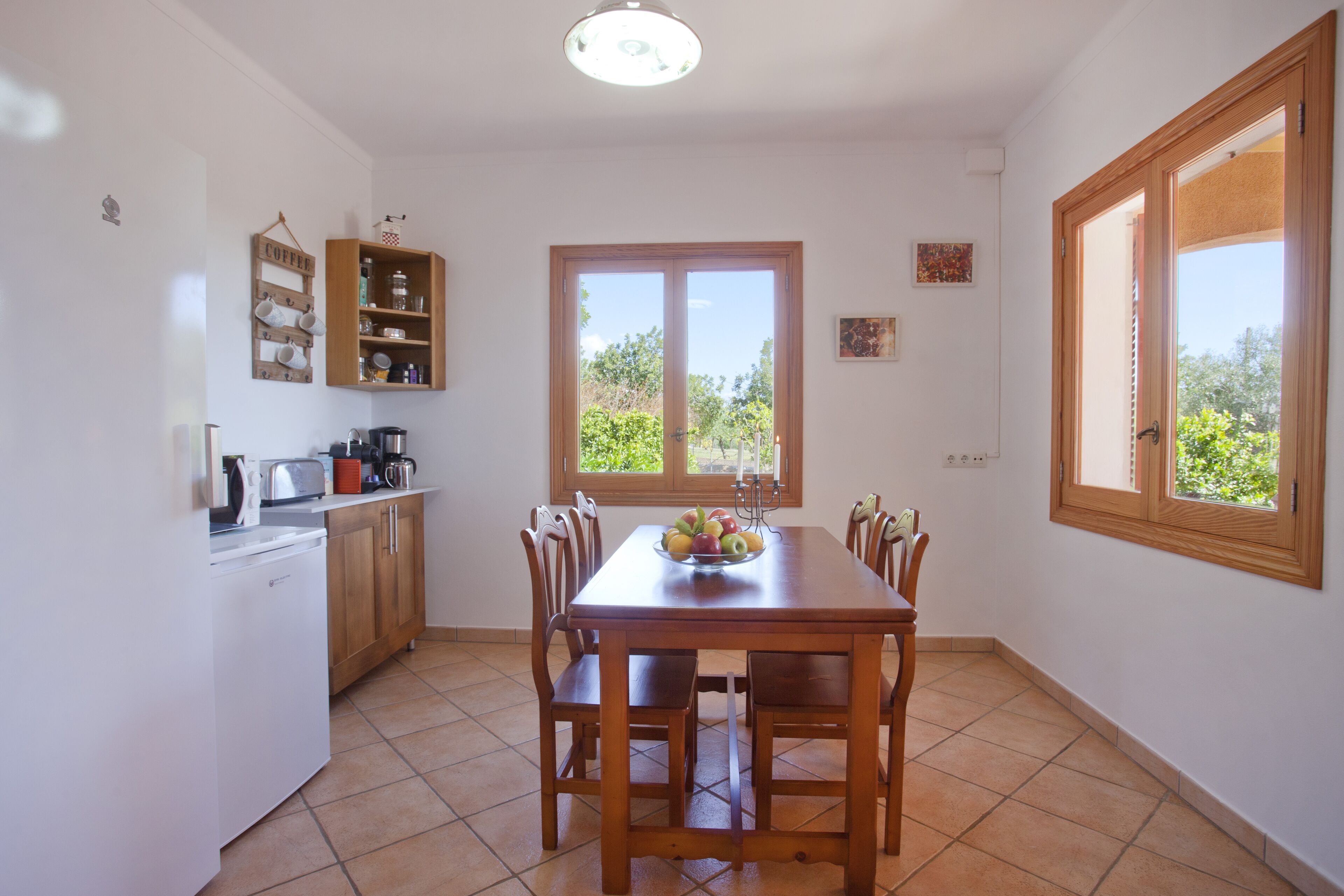 A kitchen with a dining table, chairs, a coffee shelf, and a window with a view of greenery.