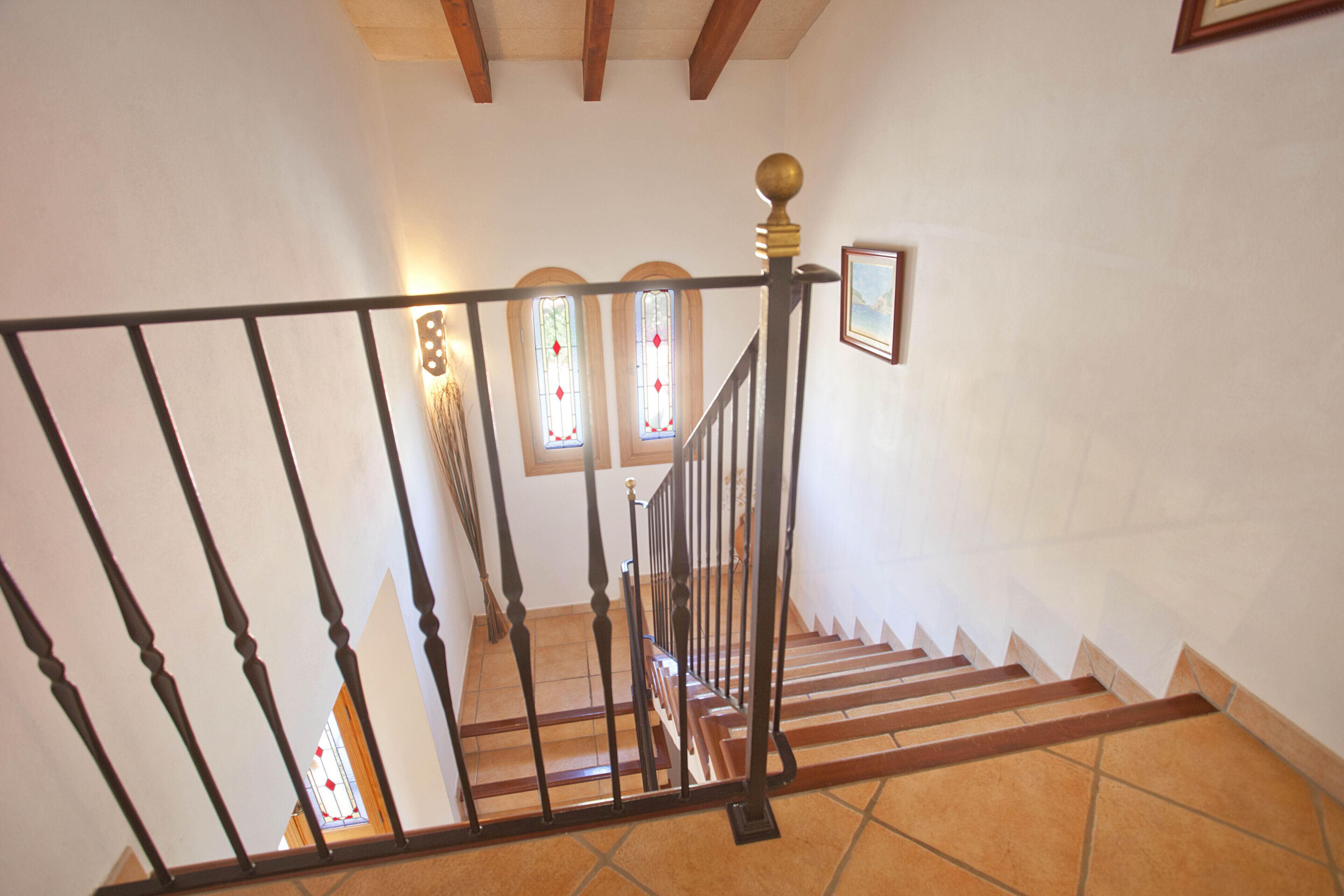 Un escalier avec une rampe noire, des marches en bois et un sol carrelé.