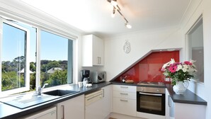 A modern kitchen with a large window, a microwave, a coffee maker, and a red accent wall. - 1 bedroom accommodation in Falmouth (Falmouth)