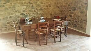 A dining area with a stone wall, wooden table, and chairs. - CA GIACOMO, in the middle of the Lunigiana woods .. relax ... and unique atmospheres (Serrapiana)