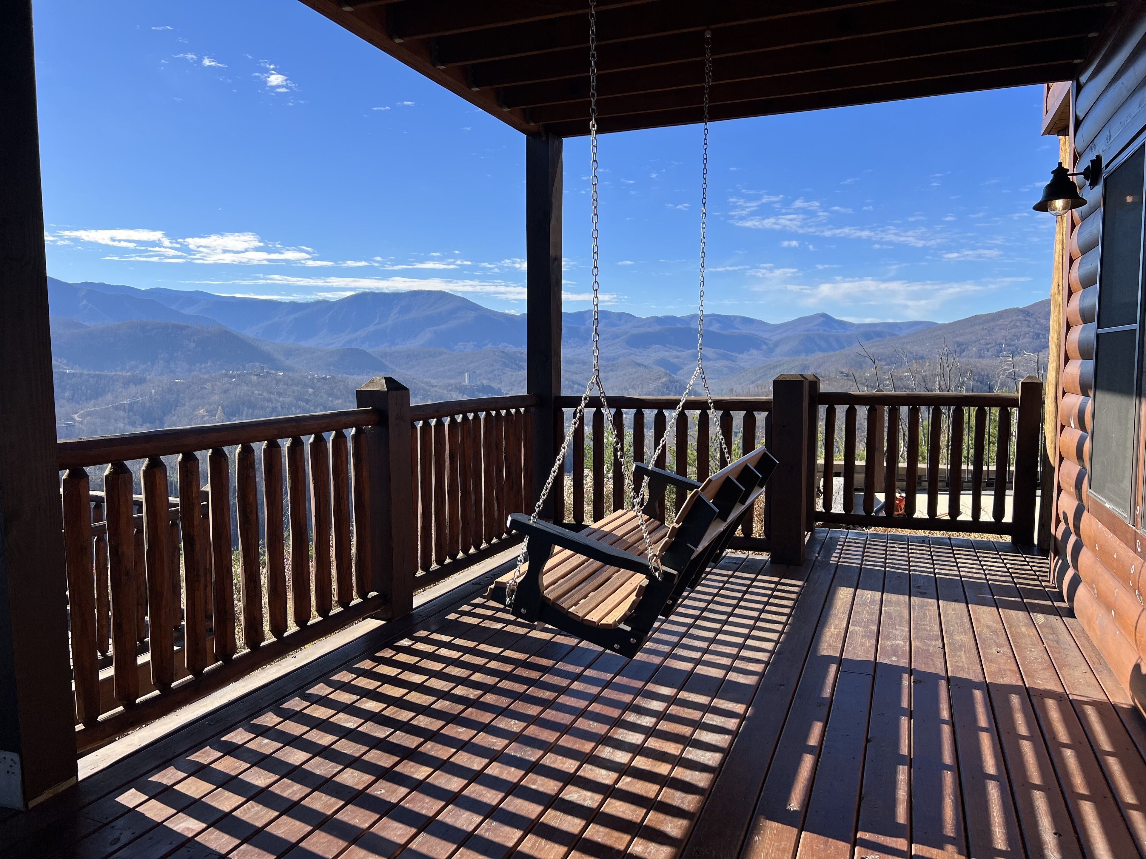A wooden deck with a swing chair overlooking a mountainous landscape.