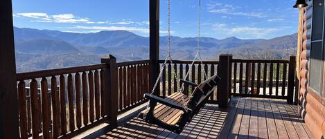 A wooden deck with a swing chair overlooking a mountainous landscape.