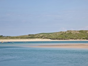 Una playa costera con barcos, una orilla arenosa y un paisaje montañoso al fondo.