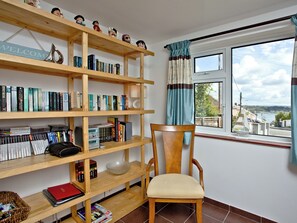 A room with a wooden bookshelf filled with books, a chair, and a window with a view of a town.