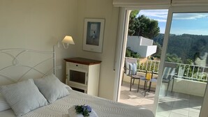 Un dormitorio con cama, mesita de noche, lámpara, un cuadro en la pared y un balcón con sillas y mesa.
