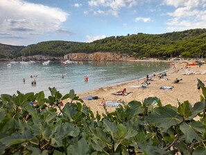 A beach with people swimming and sunbathing, boats in the water, and a hilly landscape in the background. - Comfortable villa in Punta Montgó with spectacular views,  pool and garden (L'Escala)
