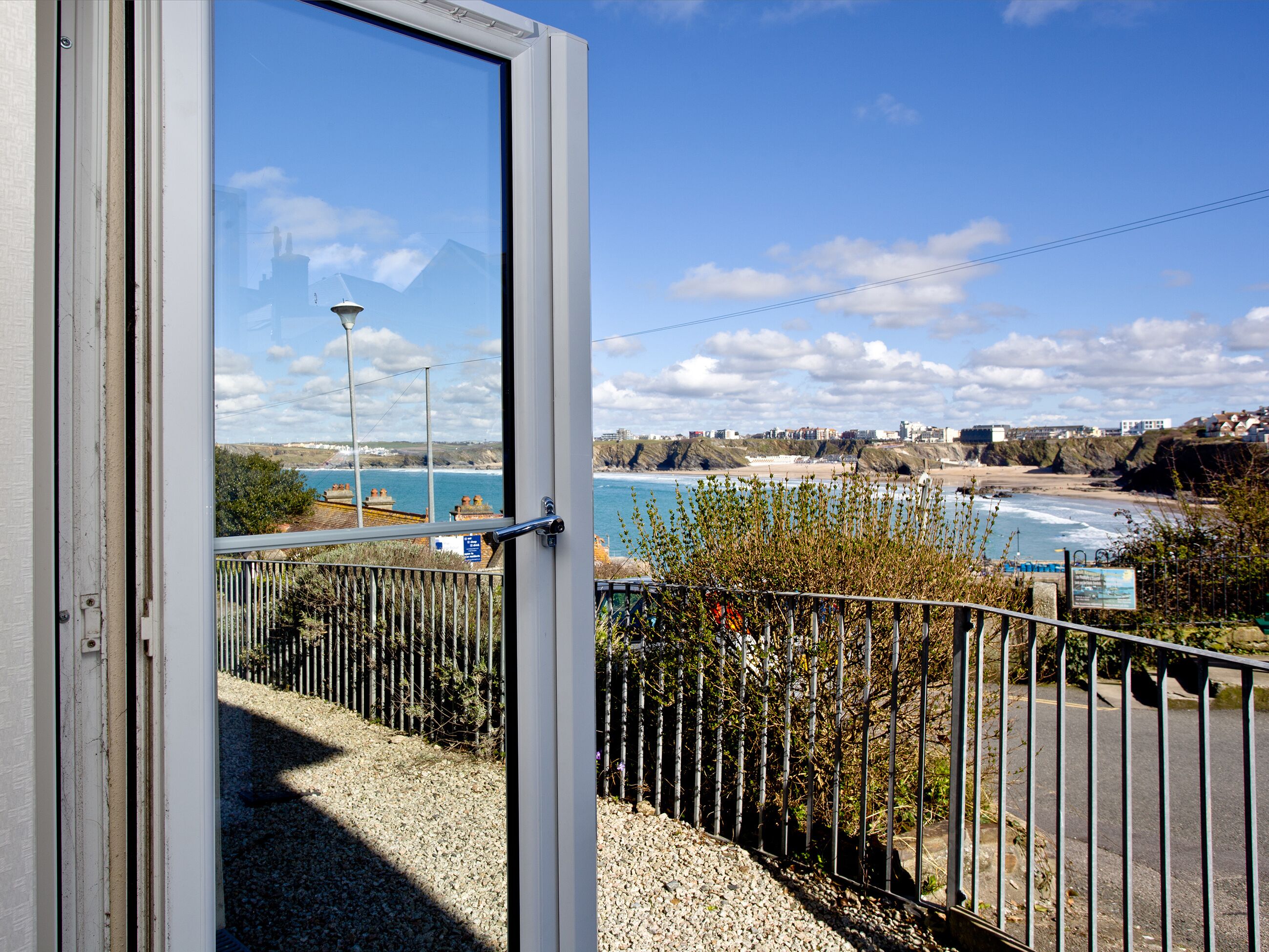 Une vue sur la côte, aperçue à travers une porte ouverte, comprenant un chemin de gravier, une clôture en métal et des bâtiments situés au loin.
