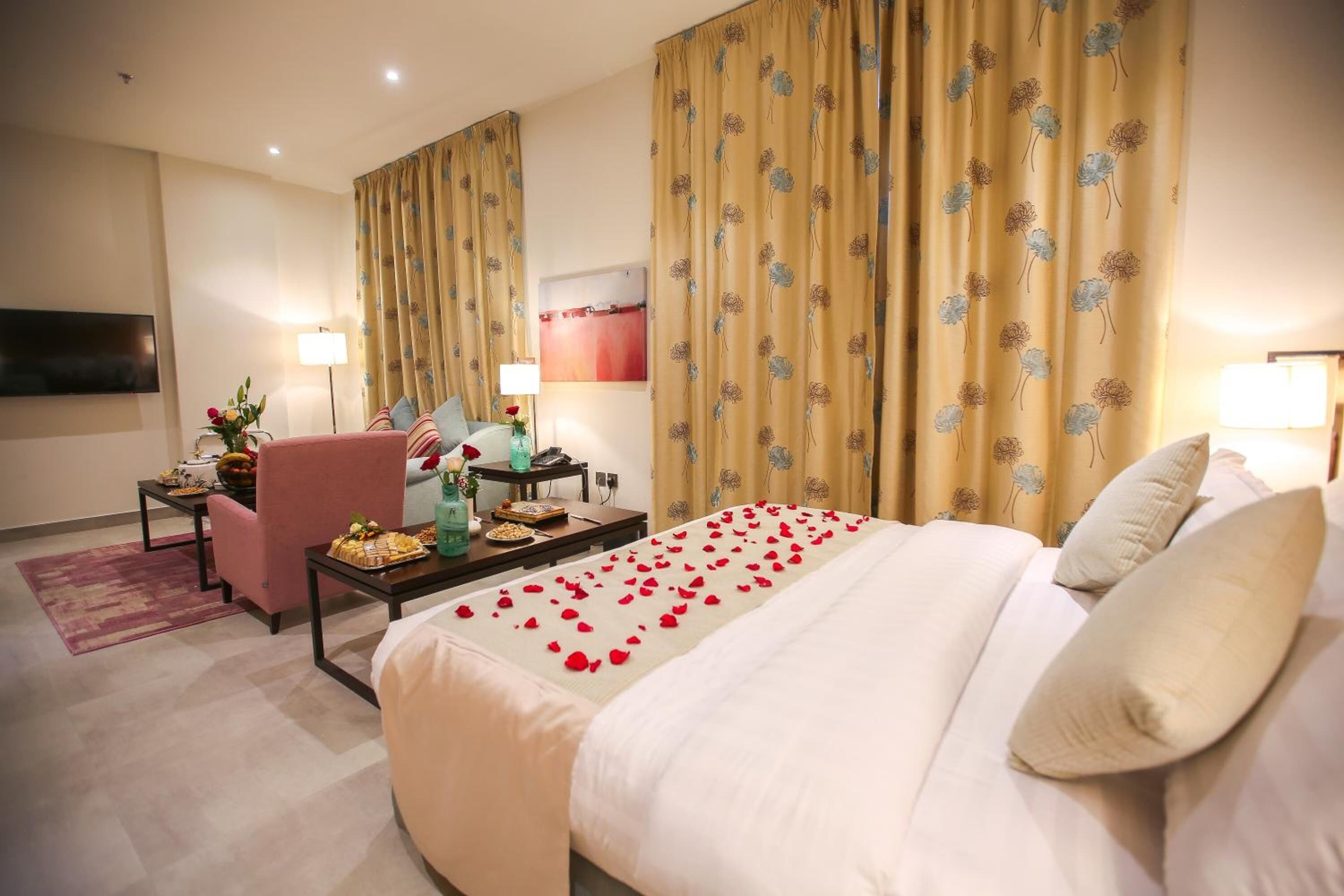 A hotel room with a bed, a desk, a chair, a TV, and curtains.